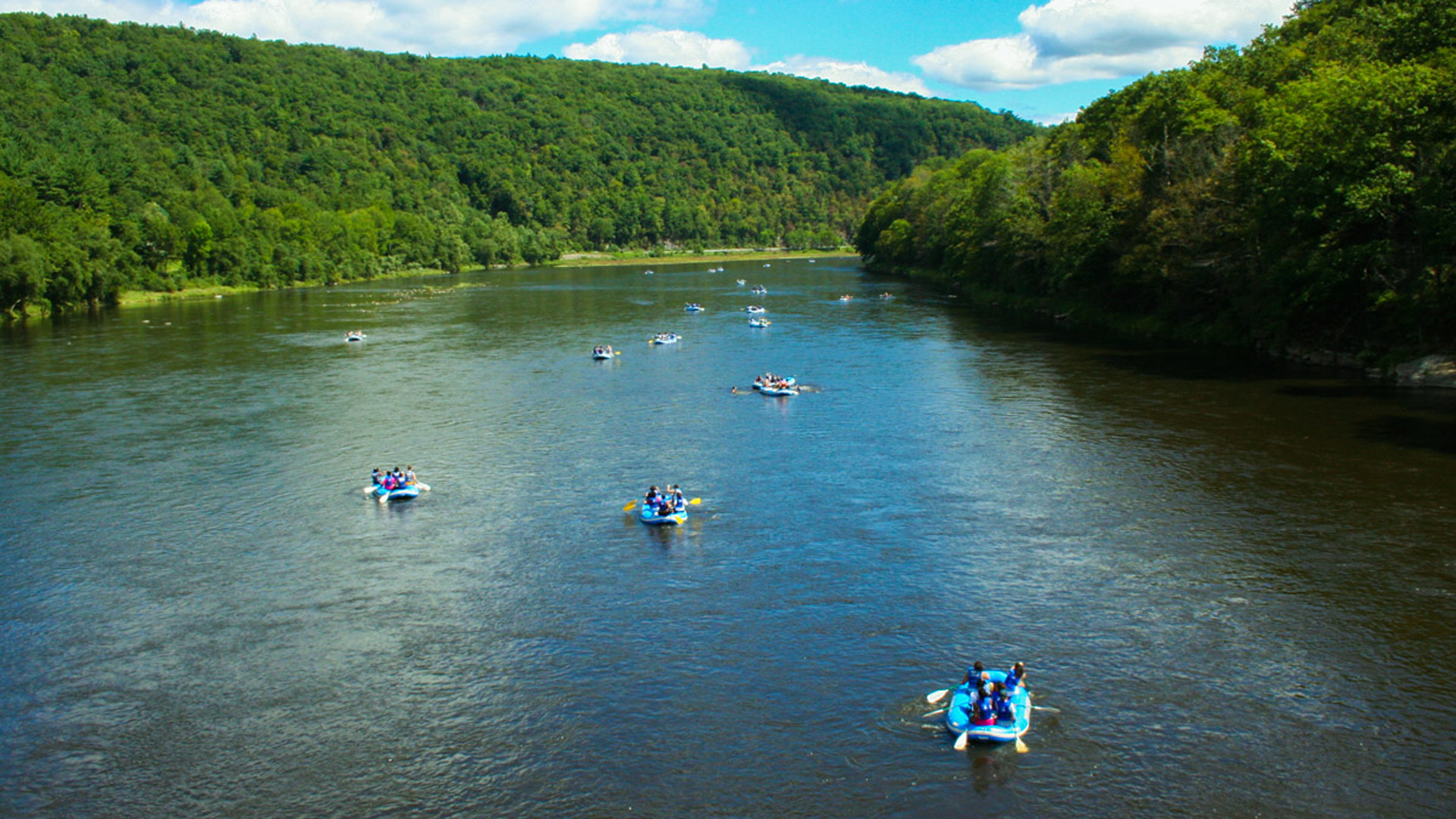 several groups on rafts on Delaware River with green tree views Indian Head Canoeing Rafting Kayaking Tubing Delaware River
